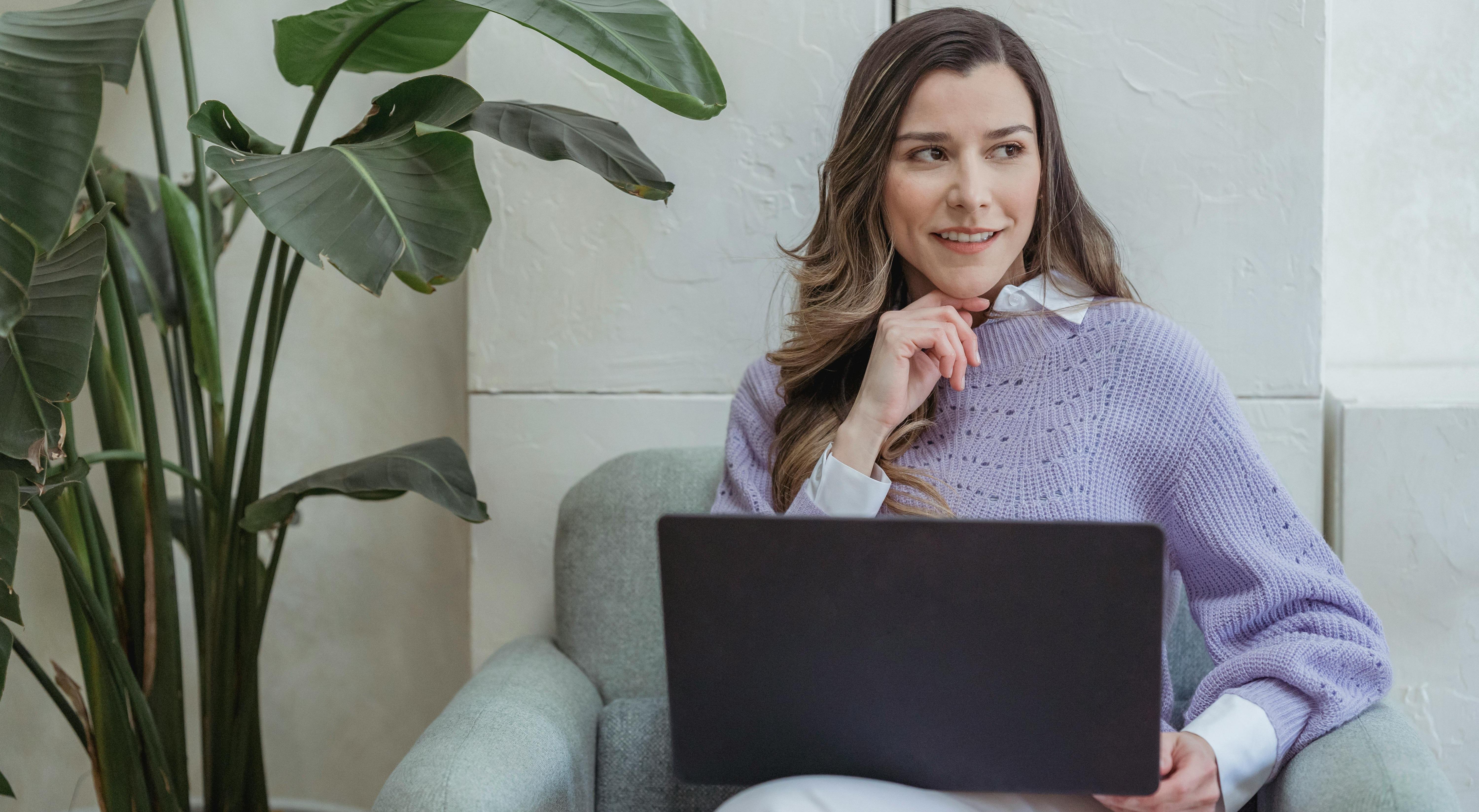 Femme pensive, ordinateur portable sur les genoux, dans un intérieur calme